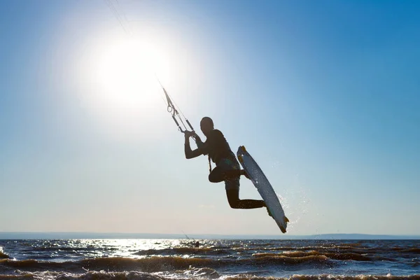 Kiteboarding. A kite surfer rides the waves. A middle-aged man enjoys riding the waves on a kite. A man is photographed opposite the sun. Silhouette.