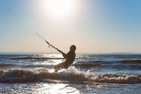 Kiteboarding. A kite surfer rides the waves. A middle-aged man enjoys riding the waves on a kite. A man is photographed opposite the sun. Silhouette.