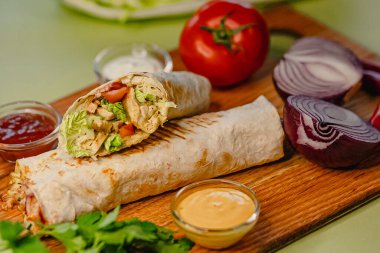 Tahta üzerinde taze sebzeler ve soslarla nefis tavuk dürümü..