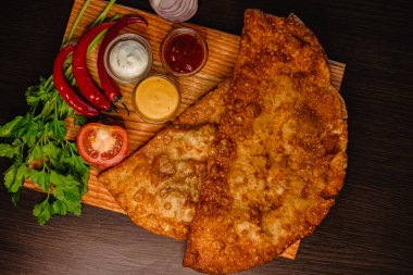 Tahtada taze otlar, domatesler ve çeşitli soslarla kızarmış chebureki..