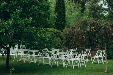 Açık havada, yemyeşil bahçedeki çimlerin üzerinde beyaz sandalyeler kurulmuş bir düğün töreni..