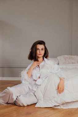 Lüks beyaz şezlonglu beyaz kadın minimalist odada yatağın yanında oturuyor..