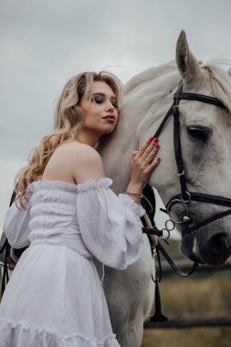 Kırsalda beyaz atı kucaklayan genç beyaz bir kadın..