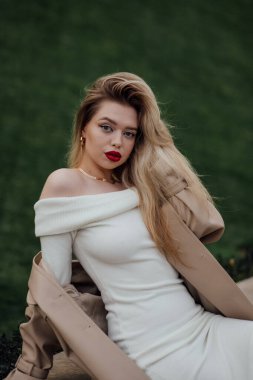 Beyaz elbiseli, açık havada poz veren zarif, beyaz bir kadın..