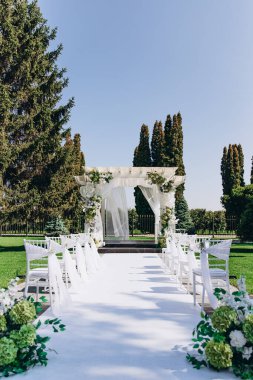 Güneşli bir günde çiçeklerle süslenmiş kemer ve sandalyelerle şık bir açık hava düğün töreni..