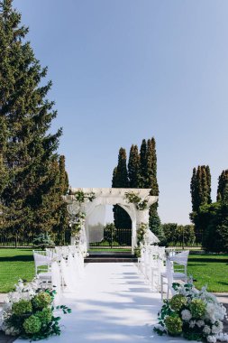 Çiçekli süslemeleri ve zarif beyaz sandalyeleri olan güzel bir açık hava düğün töreni..