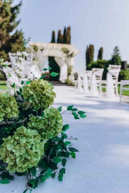 Çiçekli süslemeler ve beyaz sandalyeli şık bir açık hava düğün töreni..