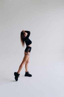 Basit bir arka planda şık siyah kıyafetli genç bir kadının modern dans ifadesi..