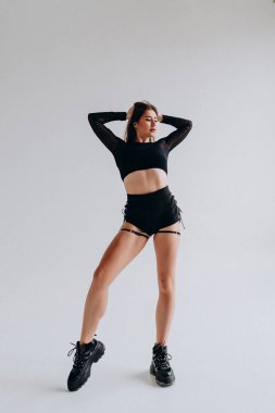 Siyah kıyafetli, minimalist stüdyo ortamında zarif poz veren kendine güvenen genç bir kadın..