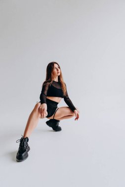 Kendine güveni tam, siyah kıyafetli bir kadın minimalist bir arka planda şık poz veriyor..