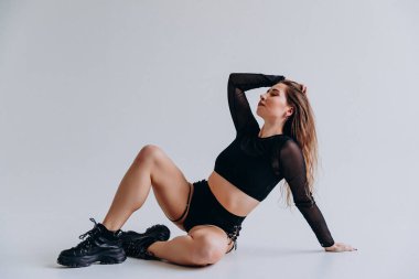 Atletik giyinmiş bir kadın minimalist bir geçmişe karşı zarif bir şekilde poz verir..