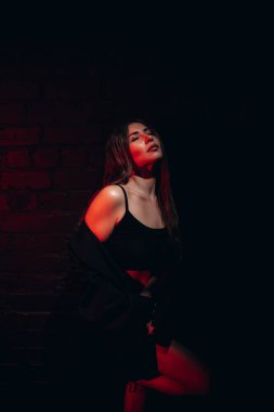 Düşünceli bir kadının karamsar portresi loş kırmızı ışık altında tuğladan bir arka planda.