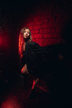 Yaratıcı ışıklandırması olan kırmızı tuğlalı duvara çarpıcı şekilde poz veren şık bir kadın..