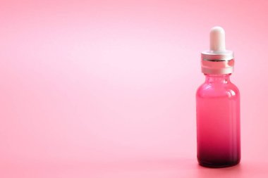 Serum şişesi. Pembe arka planda lüks pembe cam serumu şişesi..