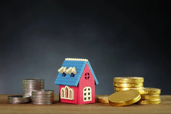 Pile of gold and silver coins with wooden house on table with dark background, copy space. Loan for real estate or money saving for buying home concepts. Loan home, real estate investment concepts.