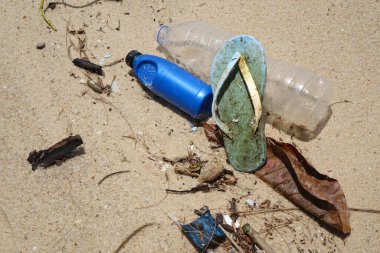 Kumsalda kirlilik. Plastik şişeler, plastik atıklar ve okyanusta ayakkabılar. Dünya çevre günü, çevre koruma kavramları. Seçici odak