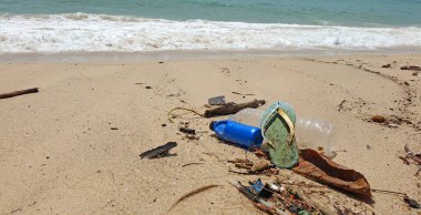 Kumsalda kirlilik. Plastik şişeler, plastik atıklar ve okyanusta ayakkabılar. Dünya çevre günü, çevre koruma kavramları. Seçici odak