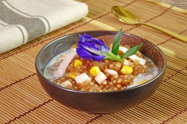 Tayland tatlısı: Tatlı mısırlı Sago Pearl, taze hindistan cevizi sütü soslu, üstünde taze hindistan cevizi eti, mavi bezelye çiçeği ve pandan yaprağı ile süslenmiş. Seçici odak.