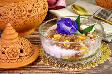 Tayland tatlısı: Tatlı mısırlı Sago Pearl, taze hindistan cevizi sütü soslu, üstünde taze hindistan cevizi eti, mavi bezelye çiçeği ve pandan yaprağı ile süslenmiş. Seçici odak.