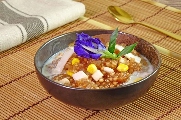 Tayland tatlısı: Tatlı mısırlı Sago Pearl, taze hindistan cevizi sütü soslu, üstünde taze hindistan cevizi eti, mavi bezelye çiçeği ve pandan yaprağı ile süslenmiş. Seçici odak.