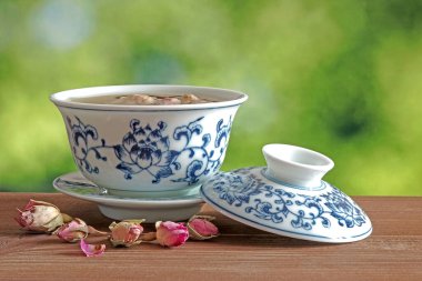 Çin usulü geleneksel mavi-beyaz porselen çay fincanı, ahşap masa üzerinde seçici odak, bulanık doğa yeşil arka plan.