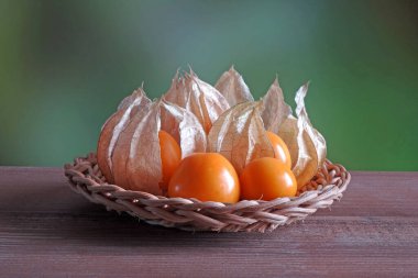 Taze Gooseberry Burnu (Physalis Peruviana) ahşap sepetin üzerinde. Kopyalama uzayı ile bulanık doğa yeşil arkaplan. Durgun hayat.