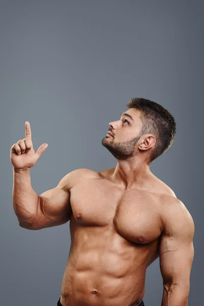 Healthy athletic young man with muscle pointing up — Stock Photo, Image