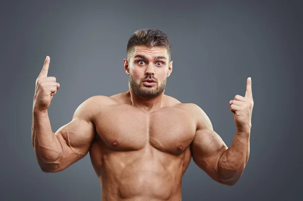 Jovem musculoso chocado apontando para cima — Fotografia de Stock