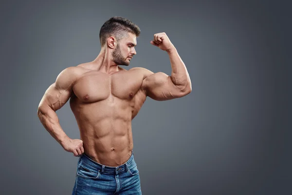 Bodybuilder poserar på grå bakgrund — Stockfoto