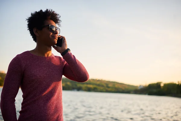 Улыбающийся чёрный мужчина разговаривает по телефону — стоковое фото