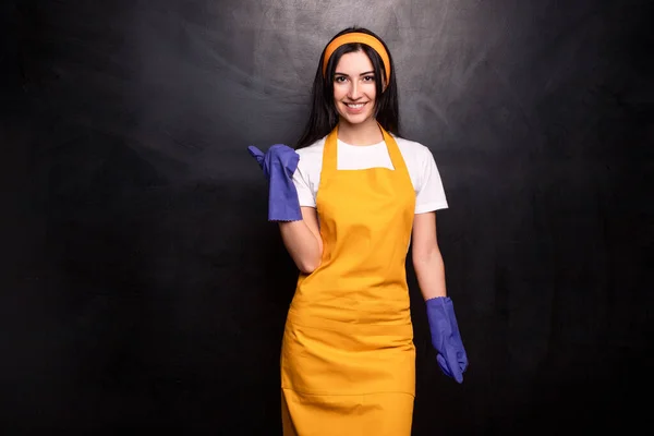 Positive Hausfrau in Schürze und Handschuhen vor schwarzem Hintergrund — Stockfoto