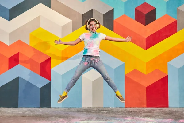 Энергичная молодая женщина в наушниках прыгает рядом с красочной стеной — стоковое фото