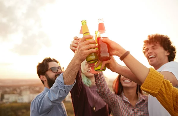 Amici felici clinking bottiglie di birra al tramonto — Foto Stock