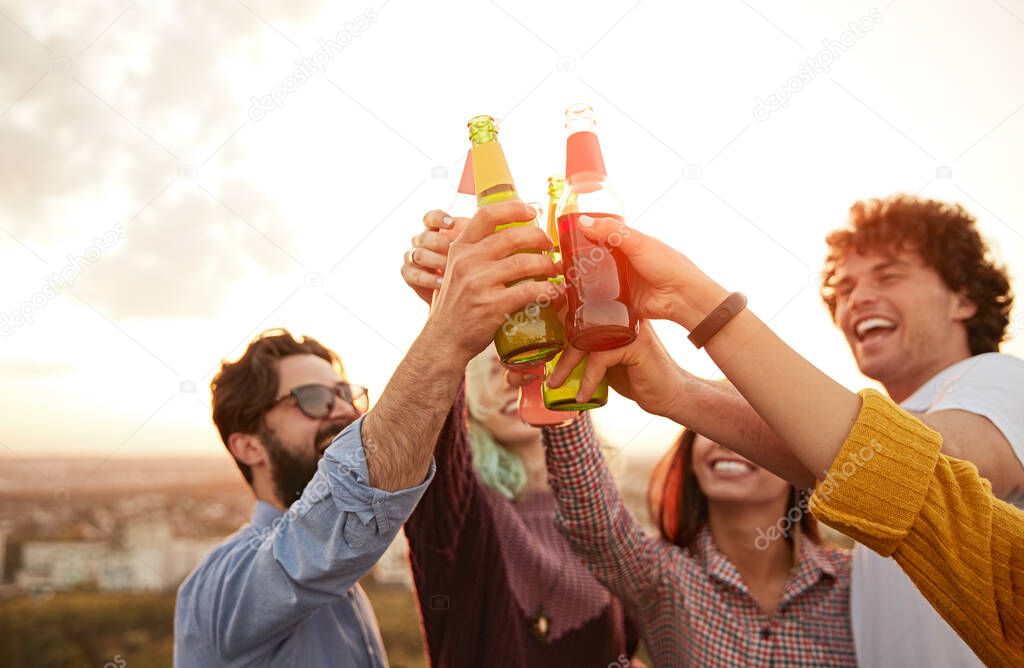 Happy friends clinking beer bottles at sunset