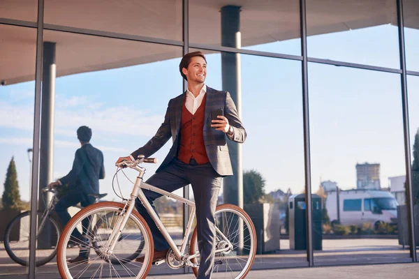 Смеющийся бизнесмен с телефоном и велосипедом на городской улице — стоковое фото