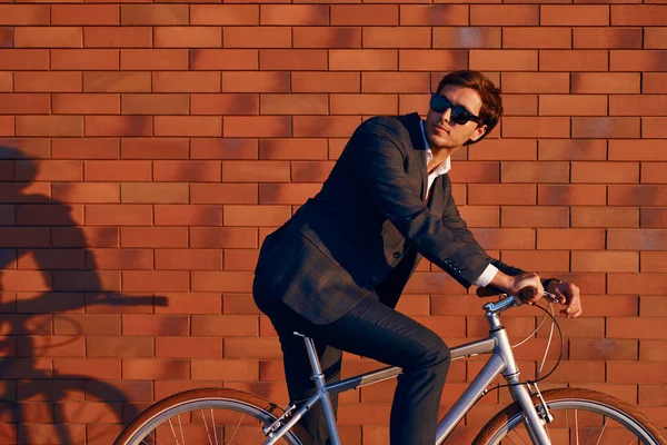 Joven empresario sentado en bicicleta contra la pared de ladrillo —  Fotos de Stock