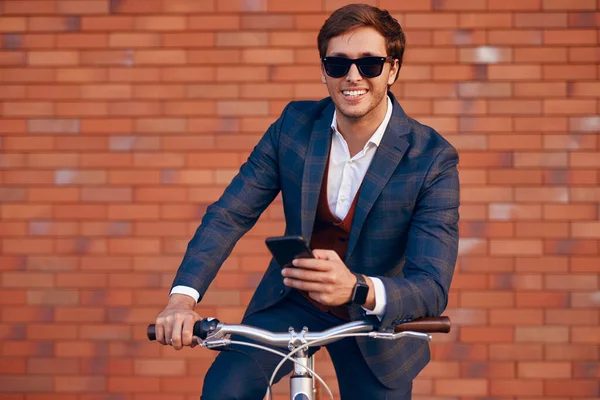 Vrolijke trendy zakenman met telefoon op de fiets — Stockfoto