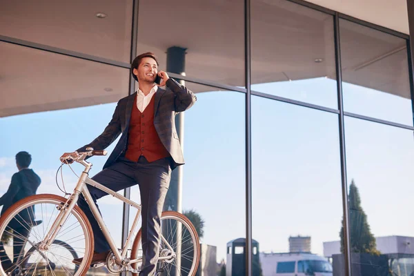 Hombre de negocios sonriente de moda hablando por teléfono sentado en bicicleta —  Fotos de Stock