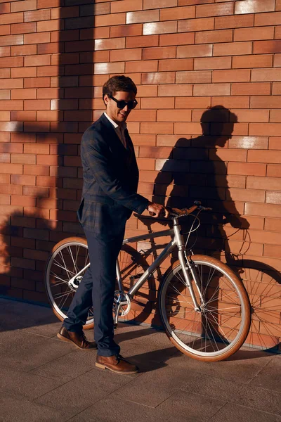 Gerente masculino con bicicleta caminando cerca de la pared de ladrillo — Foto de Stock