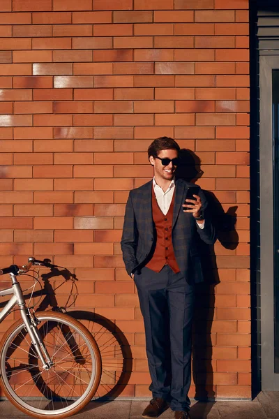 Administrador masculino exitoso usando un teléfono inteligente cerca de la bicicleta —  Fotos de Stock