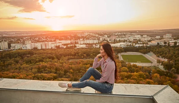 Töprengő nő ül a tetőn naplementekor — Stock Fotó