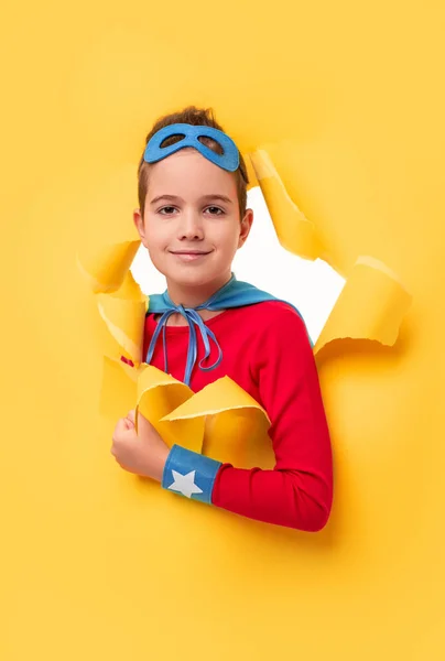Pequeno super-herói espreitando do buraco no papel amarelo — Fotografia de Stock