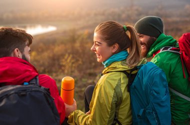 Neşeli yürüyüşçüler doğada dinlenirken termosla dinleniyorlar.