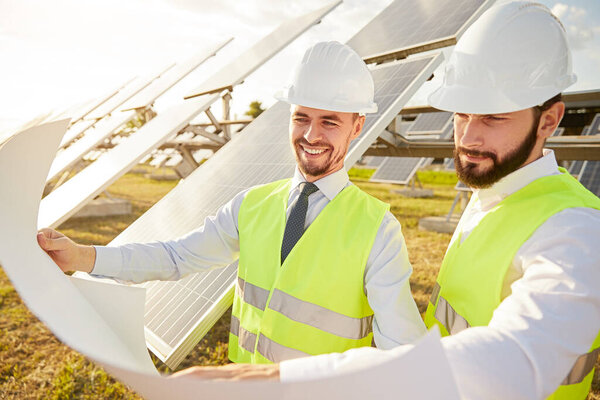 Веселые инженеры читают черновик возле солнечных панелей