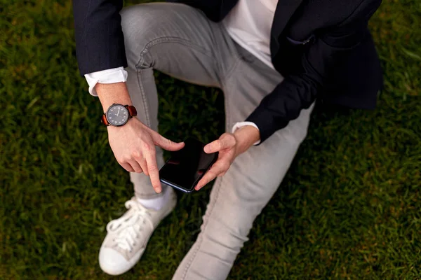 Hombre elegante sentado en la hierba y el uso de teléfono inteligente —  Fotos de Stock