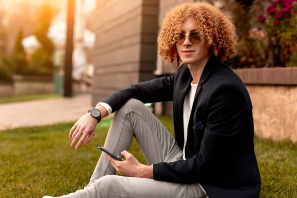 Elegante hombre con teléfono inteligente sentado en la hierba —  Fotos de Stock