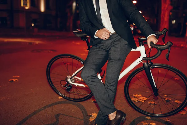 Hombre en traje formal de pie cerca de la bicicleta en la ciudad de noche —  Fotos de Stock