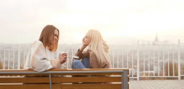 Jovens mulheres com café falando no banco — Fotografia de Stock