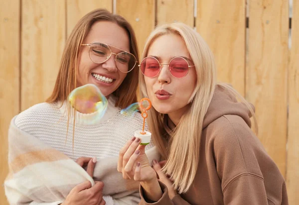 Namoradas alegres em óculos de sol elegantes soprando bolhas de sabão — Fotografia de Stock