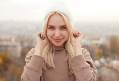 Örgü şapkalı, gülümseyen genç kadın kameraya bakıyor.